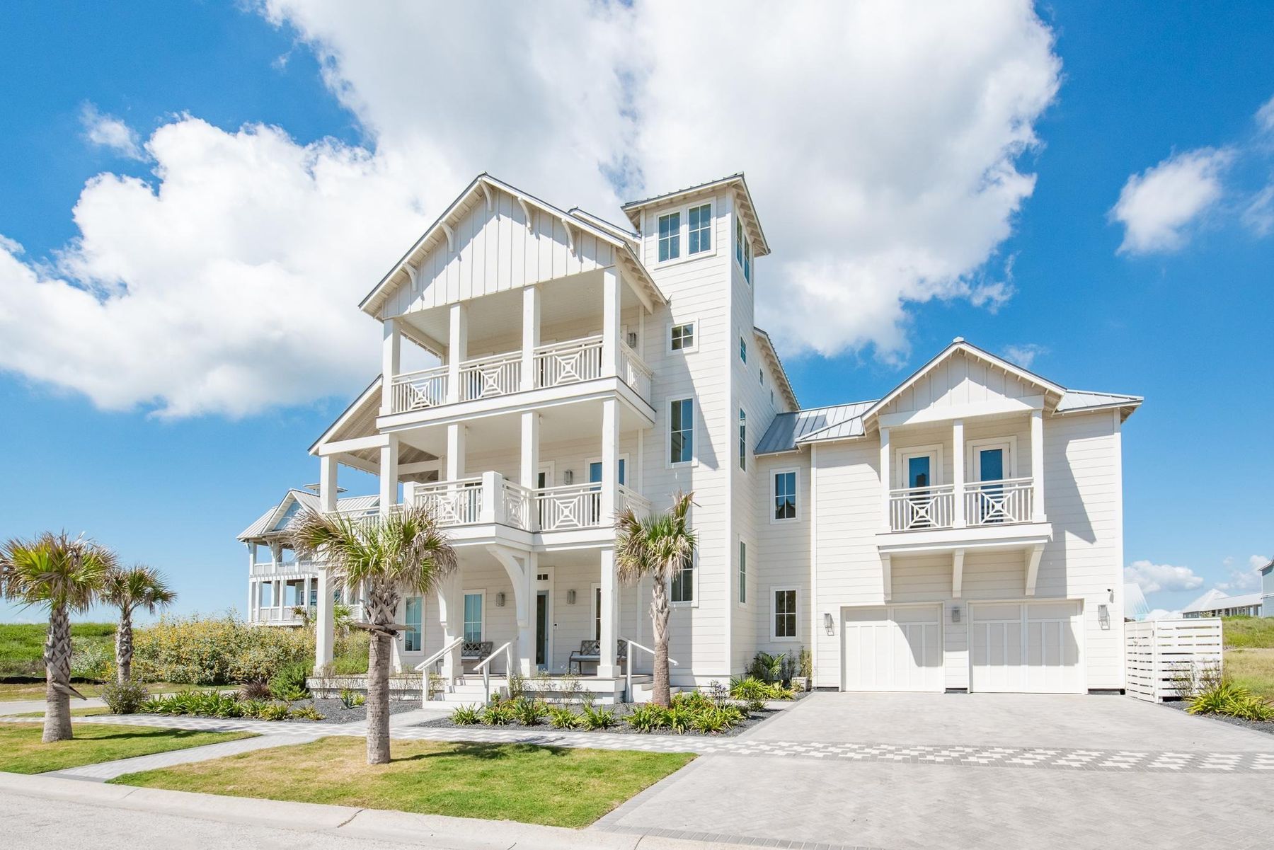 A white three-story coastal home with stacked porches and a standing-seam metal roof