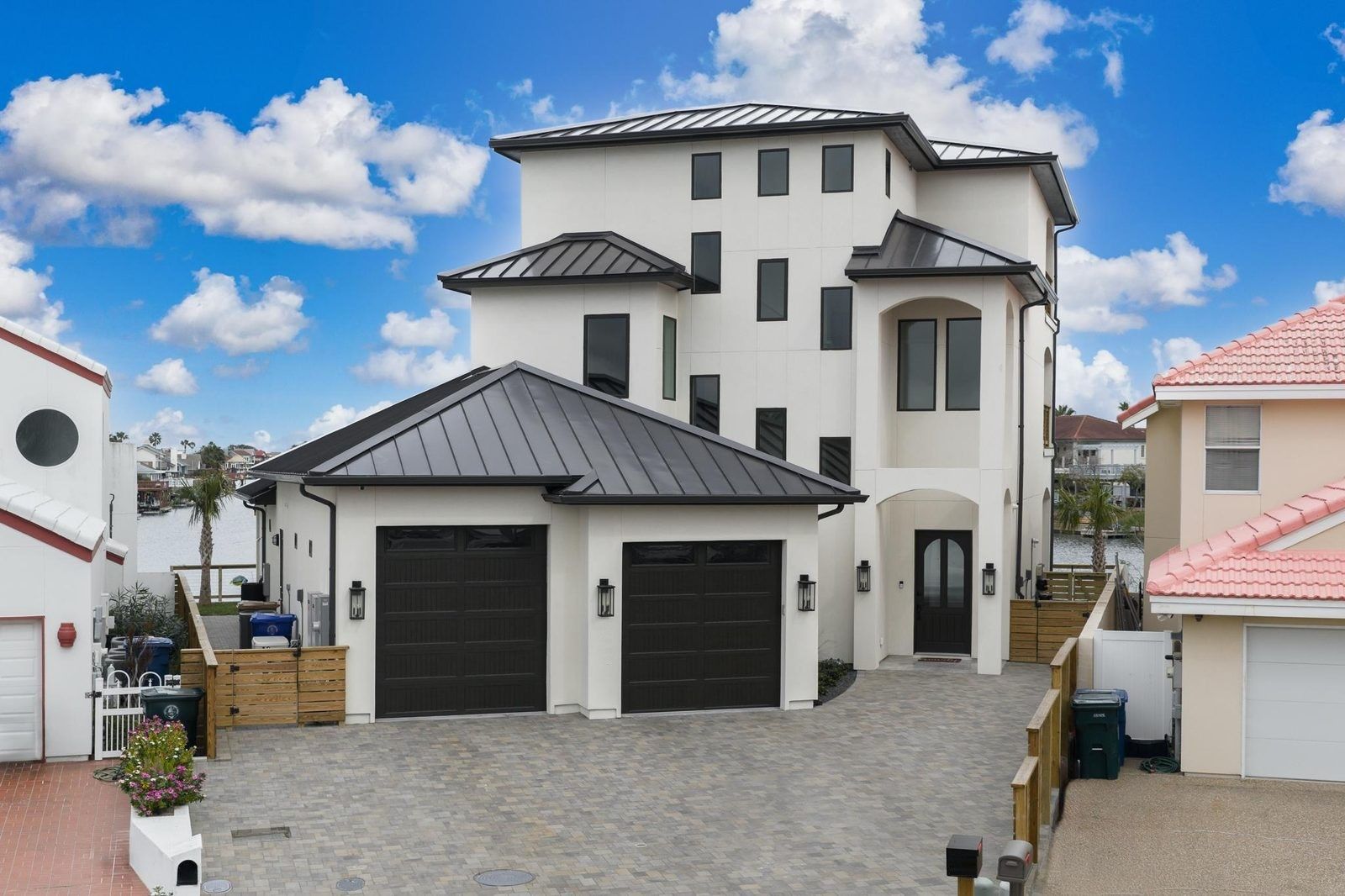 A white stucco custom home with dark garage doors, arched entry and a metal roof